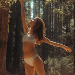 Woman wearing the Huha Mineral Bikini underwear and bralette in Tan, stretching in a sunlit forest