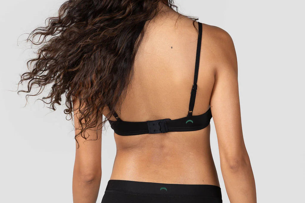 Back view of a woman with long curly hair wearing the Huha Mineral Cheeky underwear and bra in Black