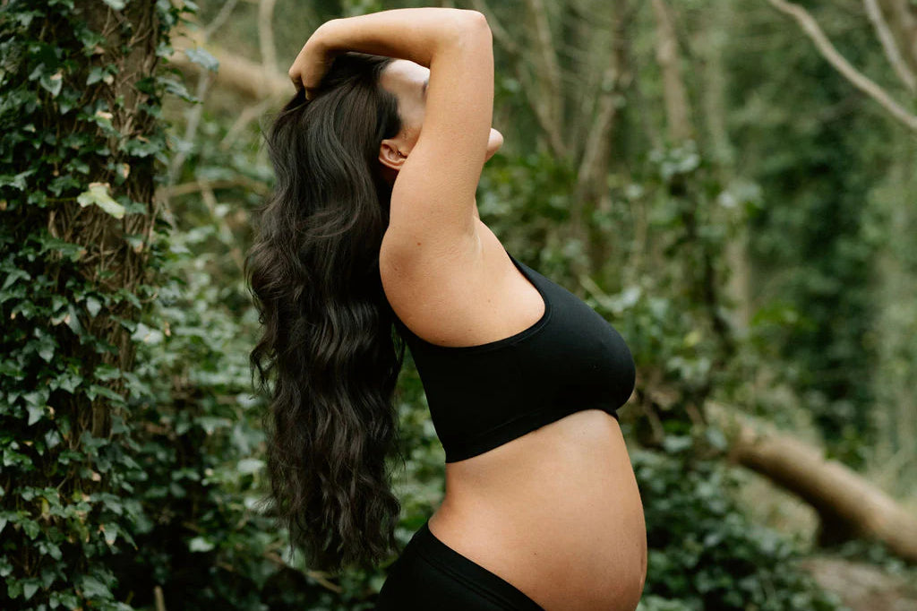 Pregnant woman in a forest wearing the Huha Mineral Cheeky underwear and bralette in Black