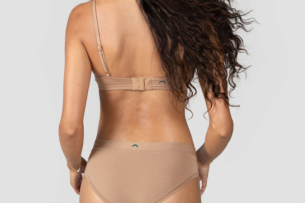 Back view of a woman with long curly hair wearing the Huha Mineral Cheeky underwear and bra in Tan