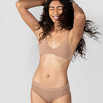 Laughing woman with curly hair wearing the Huha Mineral Cheeky underwear and bralette in Tan