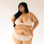 Woman with hands on hips wearing the Huha Seamless Low Mid Thong and bralette in Beige, front view