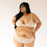 Woman with hands on hips wearing the Huha Seamless Low Mid Thong and bralette in Beige, front view