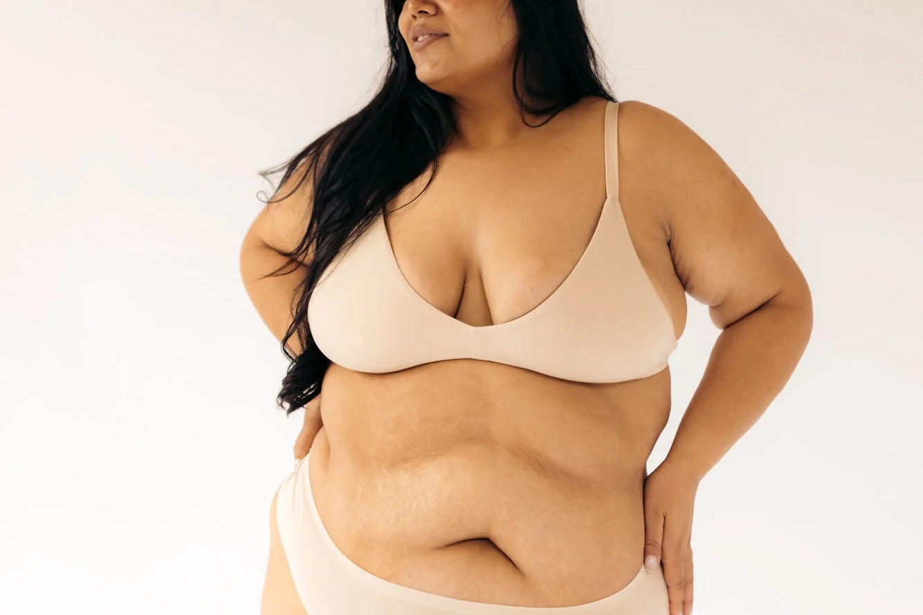 Woman with hands on hips wearing the Huha Seamless Low Mid Thong and bralette in Beige, front view