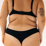 Back view of a woman wearing the Huha Seamless Low Mid Thong and bra in Black, close-up