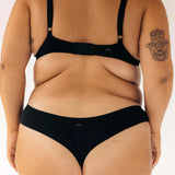Back view of a woman wearing the Huha Seamless Low Mid Thong and bra in Black, close-up