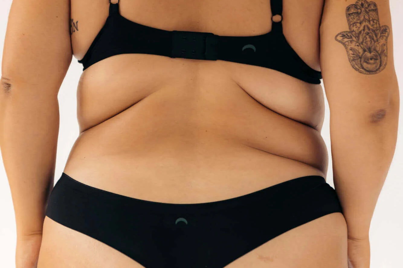 Back view of a woman wearing the Huha Seamless Low Mid Thong and bra in Black, close-up
