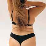 Back view of a woman with long hair wearing the Huha Seamless Low Mid Thong and bra in Black