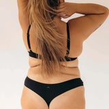 Back view of a woman with long hair wearing the Huha Seamless Low Mid Thong and bra in Black
