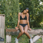 Woman sitting on a wooden fence wearing the Huha Seamless Low Mid Thong and bralette in Black