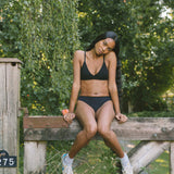 Woman sitting on a wooden fence wearing the Huha Seamless Low Mid Thong and bralette in Black