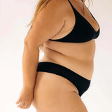 Side view of a woman wearing the Huha Seamless Low Mid Thong and bralette in Black
