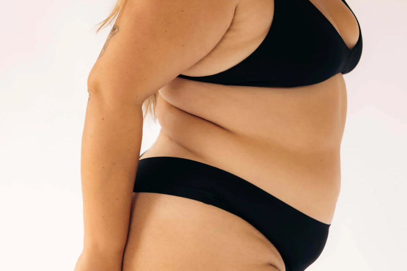 Side view of a woman wearing the Huha Seamless Low Mid Thong and bralette in Black