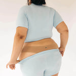 Back view of a woman in a light blue tee wearing the Huha Seamless Low Mid Thong in Tan