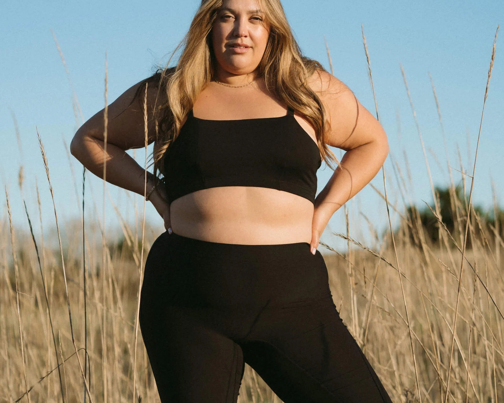 Woman standing in a field wearing the Huha Tata Bralette and bike shorts in Black, front view