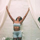 Woman with arms raised under a canopy wearing the Huha Tata Bralette and shorts in Grey