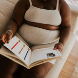 Woman reading a book while wearing the Huha Tata Bralette and underwear in Grey