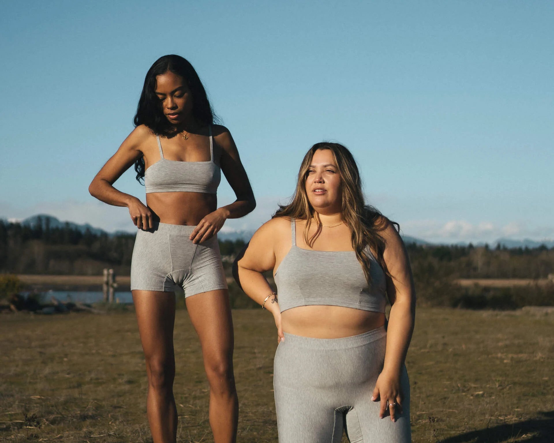 Two women in a field wearing the Huha Tata Bralette and bike shorts in Grey