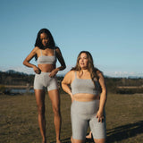Two women in a field wearing the Huha Tata Bralette and bike shorts in Grey