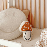 Imani Collective Mushroom Pillow in a crib beside a smiley face pillow