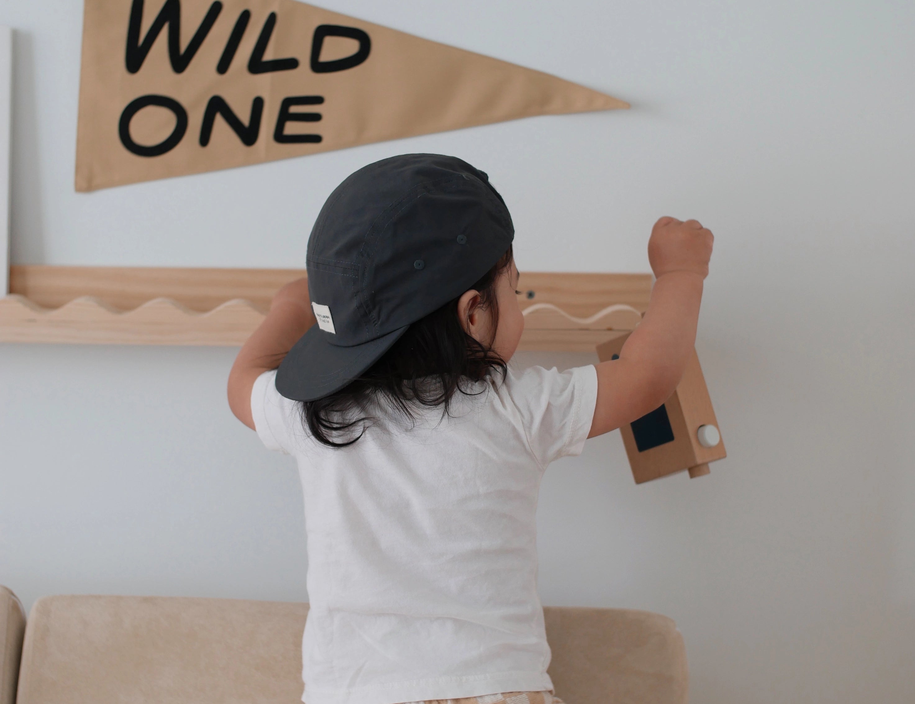 Toddler in a cap reaching up to the Imani Collective Wild One Pennant hung on a wall shelf