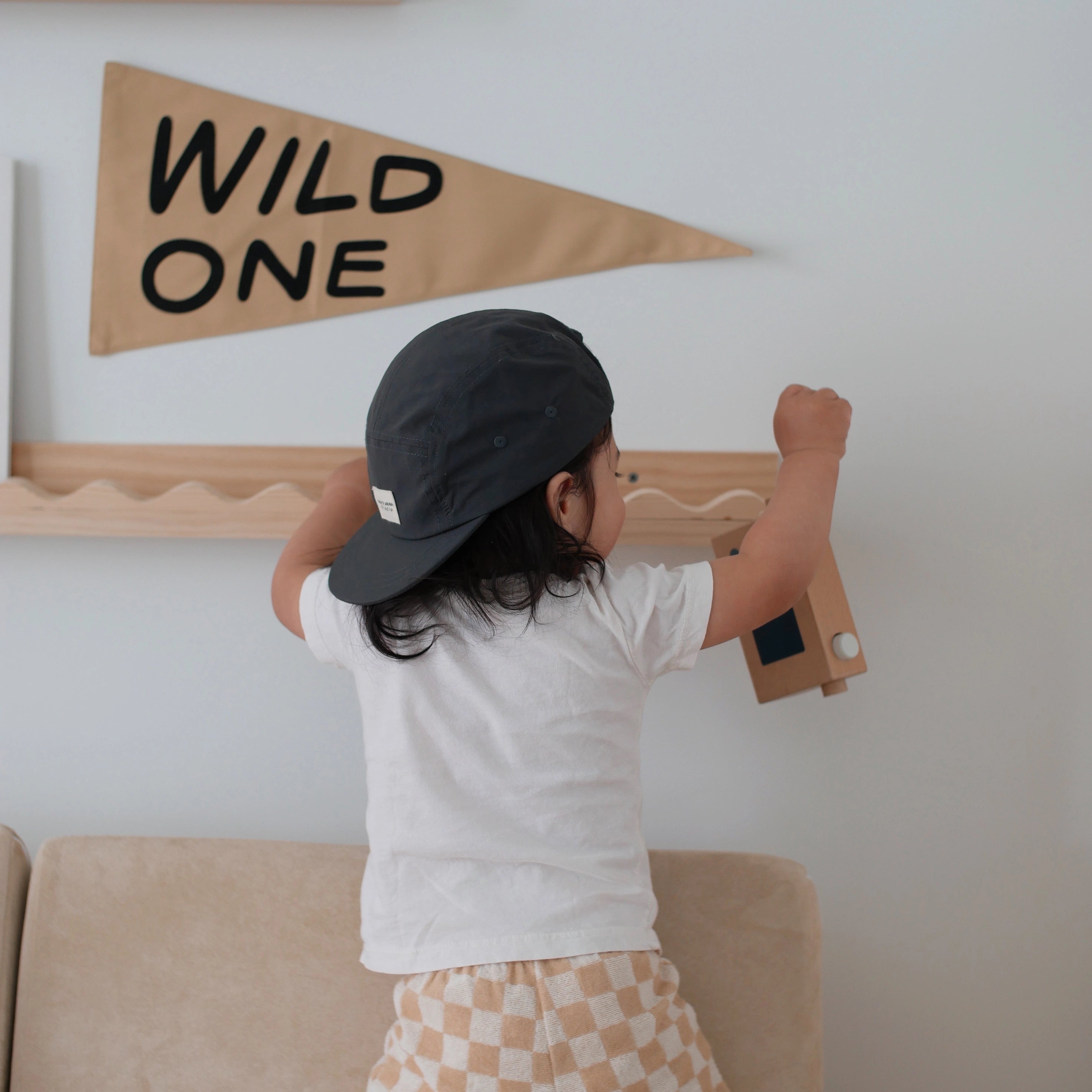 Toddler in a cap reaching up to the Imani Collective Wild One Pennant hung on a wall shelf