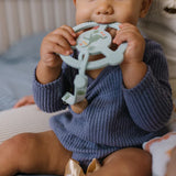 Baby in a navy sweater chewing the Jujube Roarsome Silicone Teether Ring