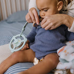 Baby holding the Jujube Roarsome Silicone Teether Ring clipped to their outfit