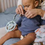 Baby holding the Jujube Roarsome Silicone Teether Ring clipped to their outfit