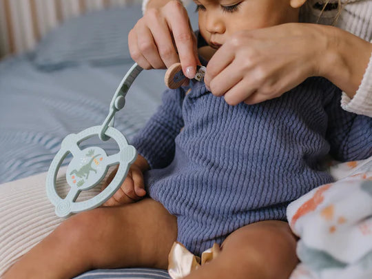 Baby holding the Jujube Roarsome Silicone Teether Ring clipped to their outfit
