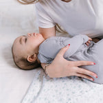 Parent laying a sleeping baby on the Jujube Roarsome Swaddle Blanket