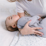 Parent laying a sleeping baby on the Jujube Roarsome Swaddle Blanket