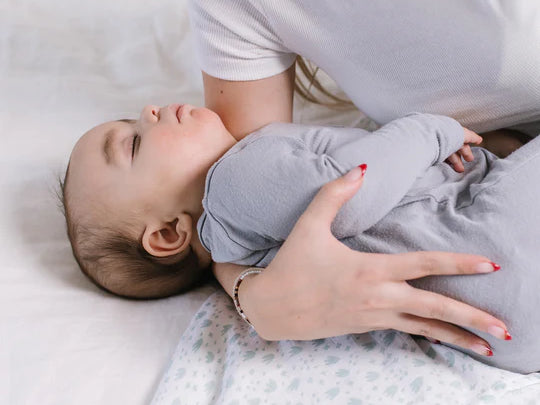 Parent laying a sleeping baby on the Jujube Roarsome Swaddle Blanket