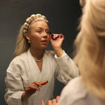 Woman in a robe doing her makeup wearing the Kaxi GRWM Headband & Wristband Set in Beige