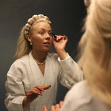 Woman in a robe doing her makeup wearing the Kaxi GRWM Headband & Wristband Set in Beige