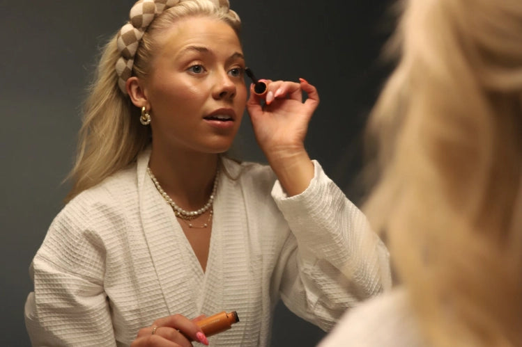 Woman in a robe doing her makeup wearing the Kaxi GRWM Headband & Wristband Set in Beige