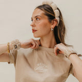 Woman in a beige tee wearing the Kaxi GRWM Headband and Wristbands in Beige, looking to the side