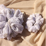 Kaxi Jumbo Coastal Cowgirl Scrunchie in periwinkle blue floral shown large and small on tan fabric