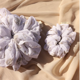 Kaxi Jumbo Coastal Cowgirl Scrunchie in periwinkle blue floral shown large and small on tan fabric