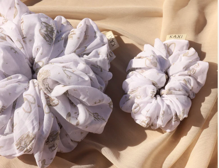 Kaxi Jumbo Coastal Cowgirl Scrunchie in periwinkle blue floral shown large and small on tan fabric