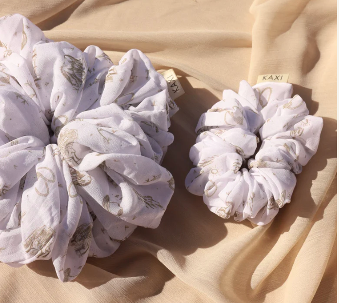 Kaxi Jumbo Coastal Cowgirl Scrunchie in periwinkle blue floral shown large and small on tan fabric