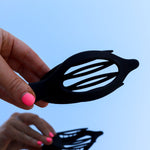 Hands holding the Kaxi Lay Down Claw 2.0 in black open against a blue sky