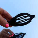 Hands holding the Kaxi Lay Down Claw 2.0 in black open against a blue sky