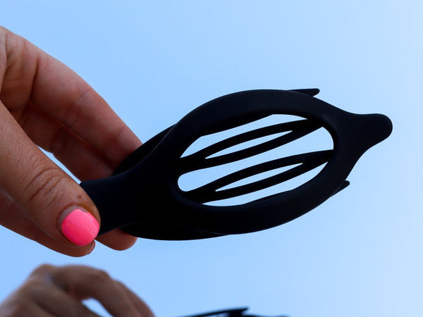 Hands holding the Kaxi Lay Down Claw 2.0 in black open against a blue sky