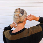Woman in a black sweater fastening the Kaxi Lay Down Claw 2.0 in clear into a twisted updo