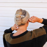 Woman in a black sweater fastening the Kaxi Lay Down Claw 2.0 in clear into a twisted updo