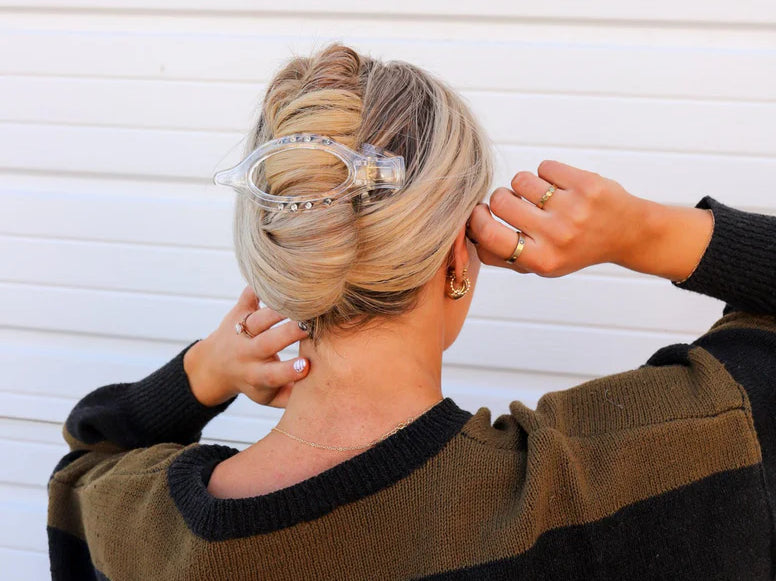 Woman in a black sweater fastening the Kaxi Lay Down Claw 2.0 in clear into a twisted updo