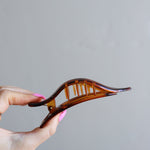 Hand holding the Kaxi Lay Down Claw 2.0 in tortoise, showing its slim curved shape