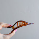 Hand holding the Kaxi Lay Down Claw 2.0 in tortoise, showing its slim curved shape