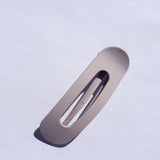 Kaxi Lay Down Claw hair clip in matte taupe, a flat rectangular claw clip on a blue background